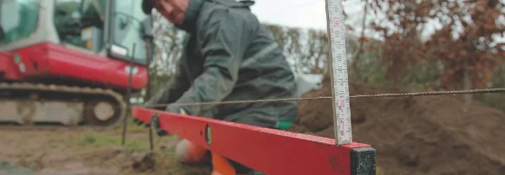 Person nutzt eine rote Wasserwaage und eine Schnur, um die Höhe präzise zu prüfen.